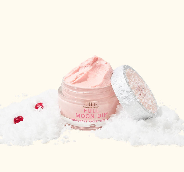 FarmHouse Fresh Full Moon Dip Illumination Mousse body moisturizer styled in snow with festive holiday greenery and red berries