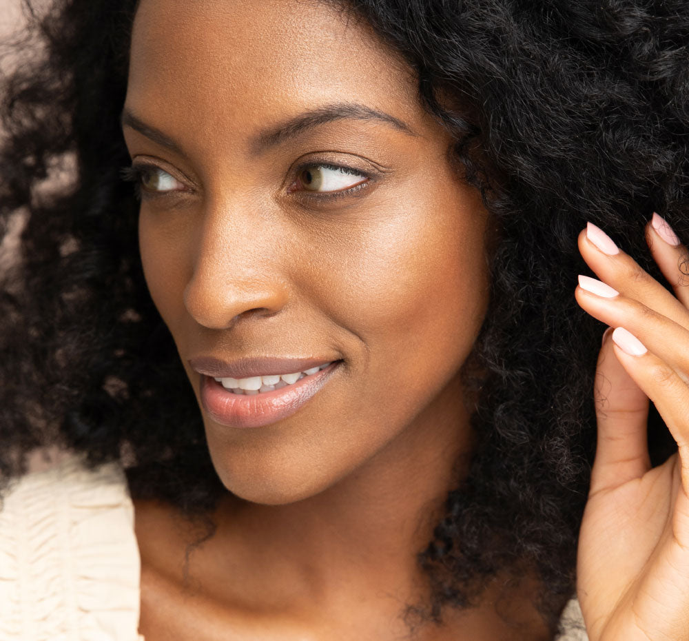 A woman is demonstrating her beautiful complexion with a golden glow after using FarmHouse Fresh Golden Moon Dip Illumination Face Mousse with Retinol and Wrinkle-Targeting Peptides.