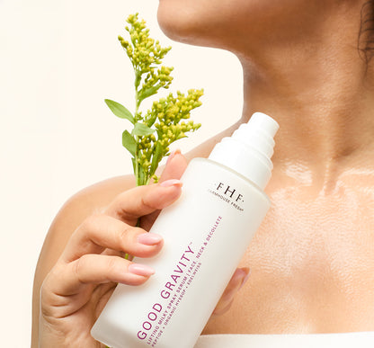 Woman holding a bottle Good Gravity Lifting Milky Spray Serum against chest with visibly hydrated skin.