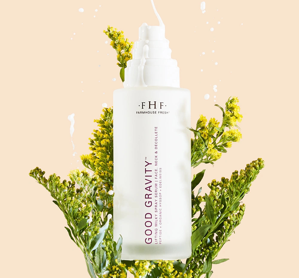Bottle of Good Gravity Lifting Milky Spray Serum in a bundle of flowers with serum dripping on bottle.