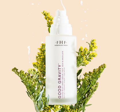Bottle of Good Gravity Lifting Milky Spray Serum in a bundle of flowers with serum dripping on bottle.