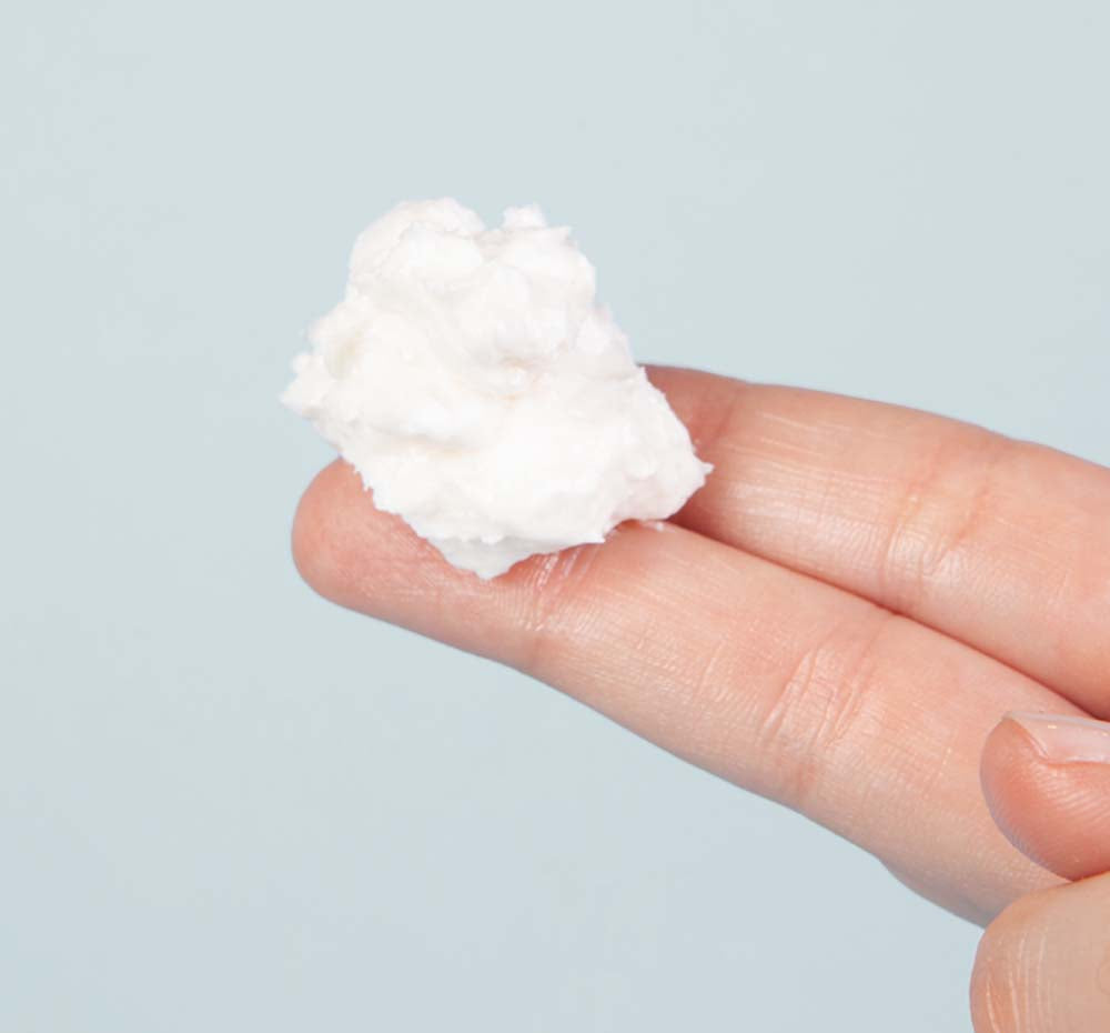 A hand holding a dollop of Harvest Moon Dip Body cream by FarmHouse Fresh showing the whipped, light texture of the body mousse.