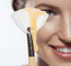 A woman is holding a Farmhouse Fresh brush with Honey Heel Glaze, a golden serum used to moisturize during a pedicure.