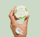 A woman's hand holding a jar of Mint Condition Hand Balm containing peptides that softening in the look of unevenness on hands
