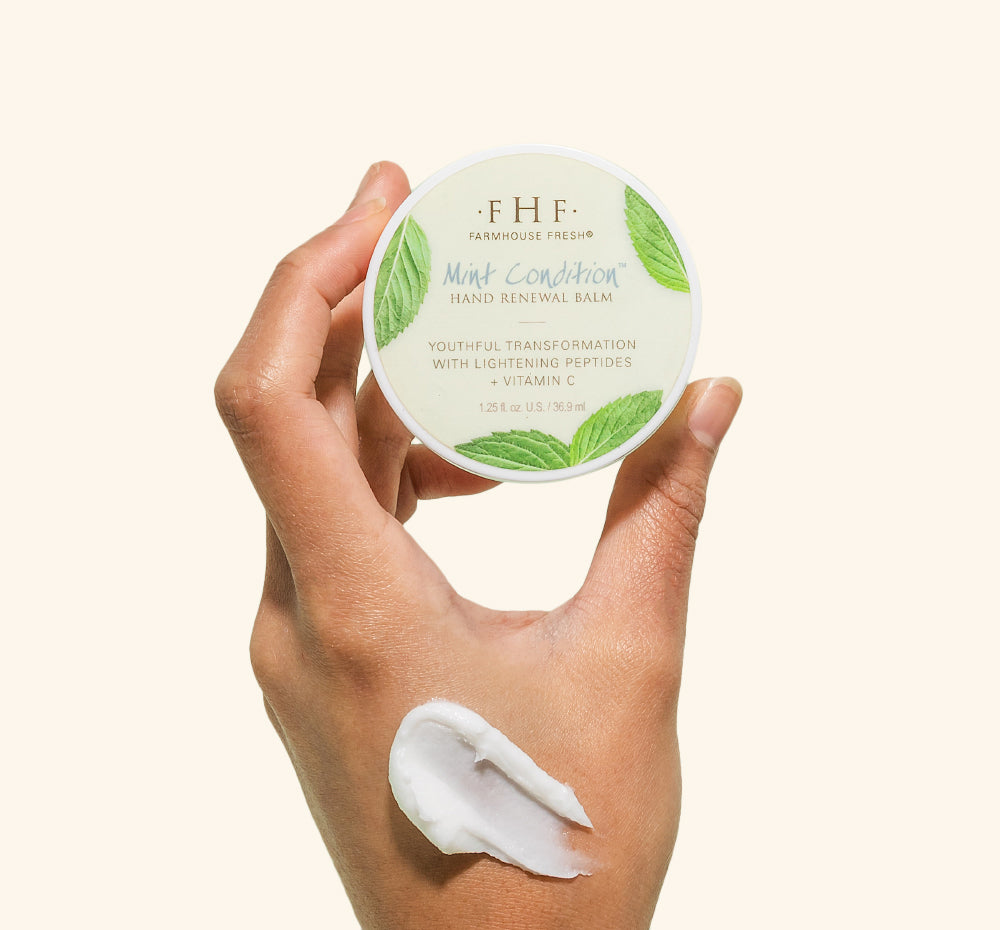 A woman's hand holding a jar of Mint Condition Hand Balm containing peptides that softening in the look of unevenness on hands