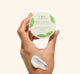 A woman's hand holding a jar of Mint Condition Hand Balm containing peptides that softening in the look of unevenness on hands