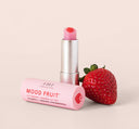 A tube of all-natural FarmHouse Fresh Strawberry Mood Fruit Lip Therapy balm next to a strawberry.