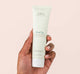 A hand holding a tube of FarmHouse Fresh Moon Dip Ageless Mousse for Hands with age defying ingredients.