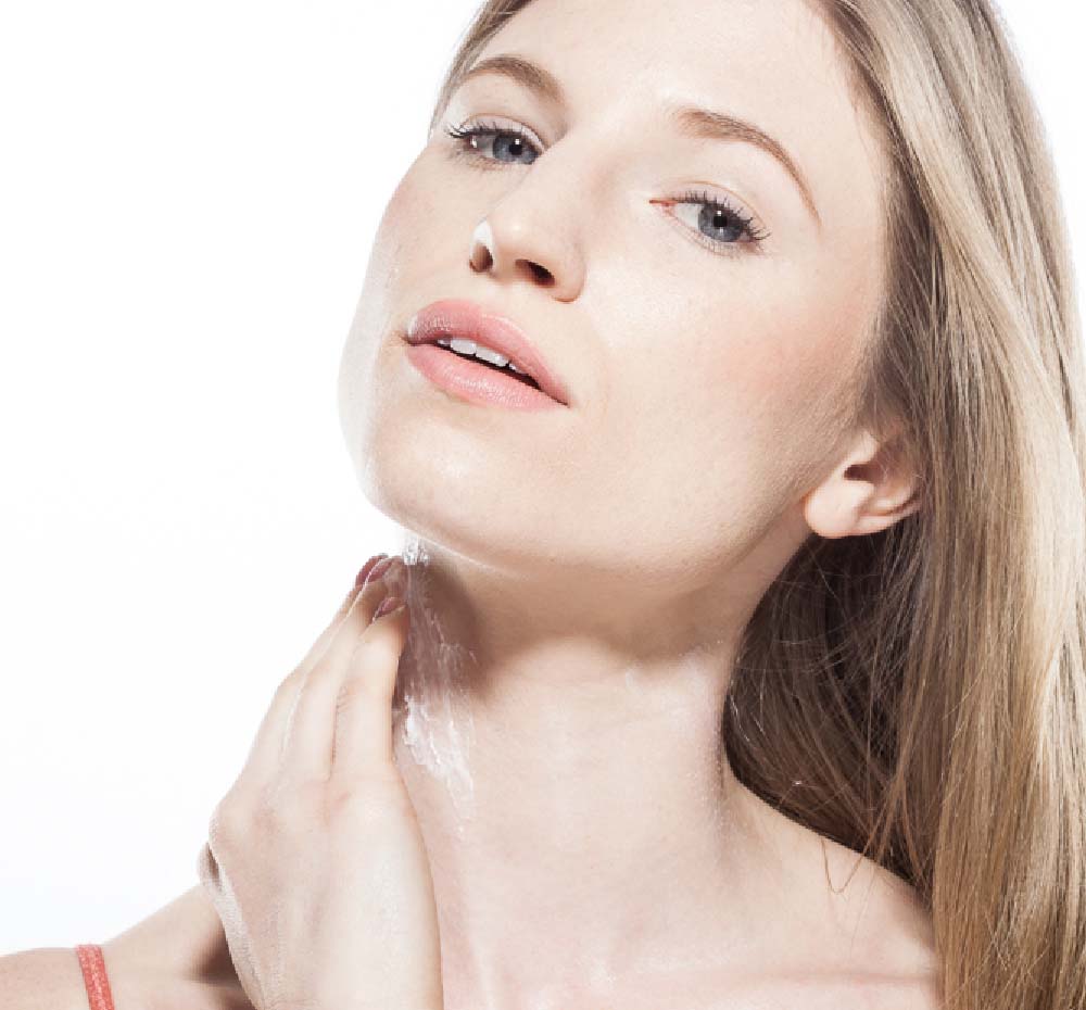 A woman applying FarmHouse Fresh Moon Dip Body Mousse for aging skin on her neck to smooth the look of wrinkles.