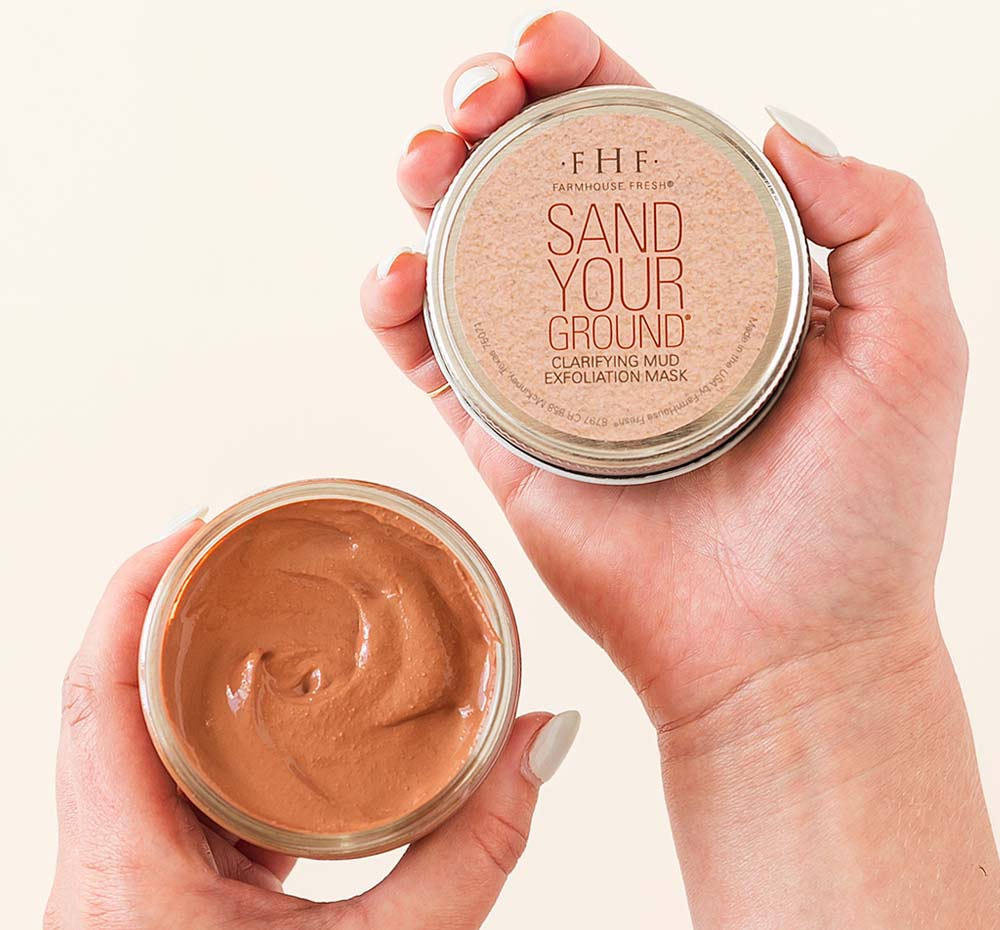 Hands holding a jar of Farmhouse Fresh Sanded Ground Clarifying Mud Exfoliation Mask for acneic, blemish-prone and oily skin.