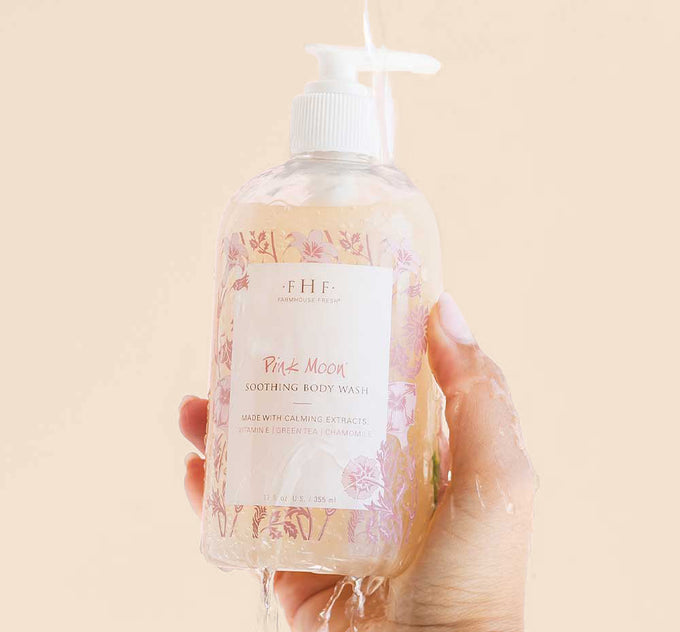 A hand holding a bottle of gentle Pink Moon Body Wash body wash for sensitive skin by Farmhouse Fresh.