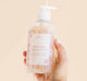 A hand holding a bottle of gentle Pink Moon Body Wash body wash for sensitive skin by Farmhouse Fresh.