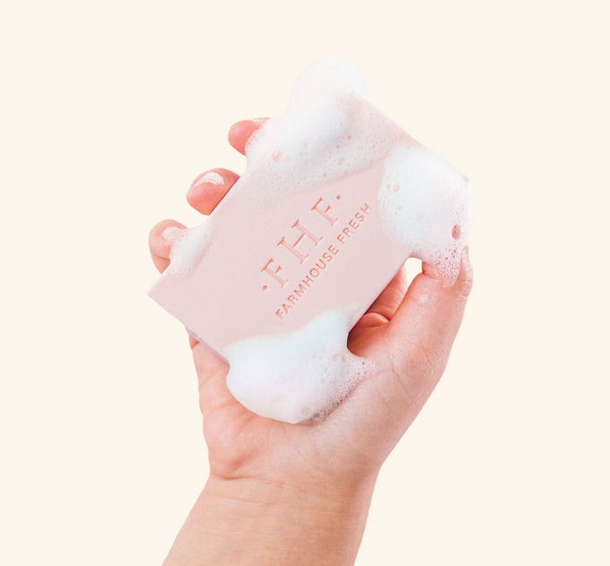 
A hand holding a bar of softly scented FarmHouse Fresh Pink Moon Shea Butter Bar Soap with rich lather on it.
