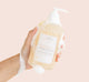 A hand holding a lather-covered bottle of Farmhouse Fresh Rainbow Road® Body Wash made with made with aloe, vitamin E and a blend skin-soothing extracts.