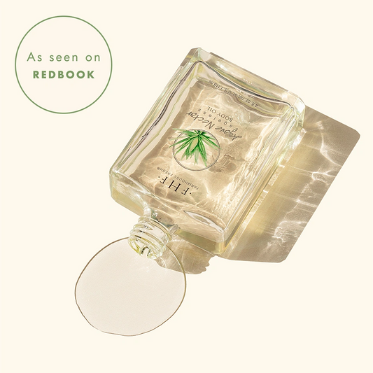 A clear bottle of Agave Nectar Body Oil lies on its side with a small pool of body oil in front, photographed on a warm off-white background. A badge reads 'As seen on REDBOOK' appear in the upper left.