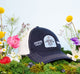 FarmHouse Fresh Smurfin' Cool Trucker Hat surrounded by flowers. All profits are donated to animal rescue initiatives around the country.