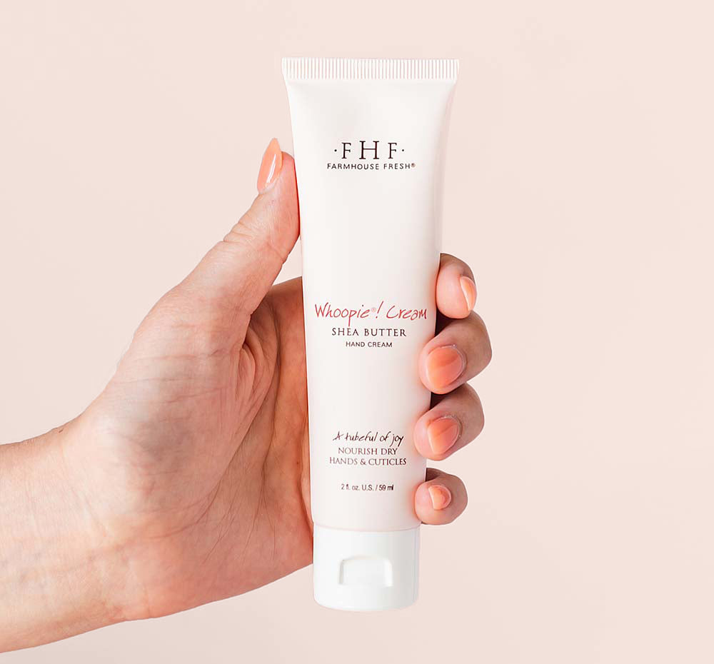 A hand holding a tube of Farmhouse Fresh Whoopie shea butter hand cream for dry skin.