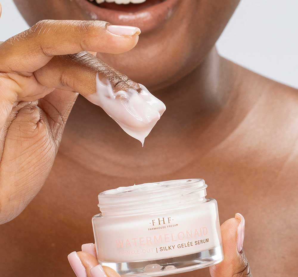 A woman is dipping her fingers into a jar of Watermelonaid face serum with CBD by FarmHouse Fresh made with hemp and watermelon extract.