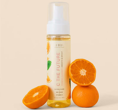 A bottle of FarmHouse Fresh C the Future Foam Facial Cleanser next to oranges that represent the natural ingredients full of vitamin C.