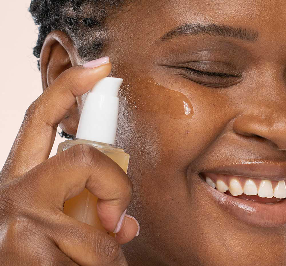 A woman is applying FarmHouse Fresh Supremely Lit Serum-in-Oil with CBD to moisturize and soften her skin.