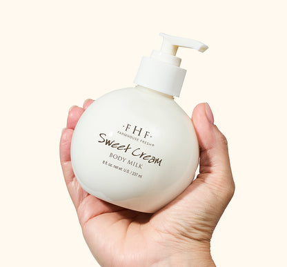 A hand holding a bottle of FarmHouse Fresh Sweet Cream Body Milk Lotion with a pump top.