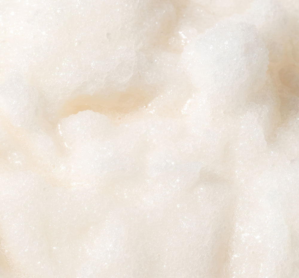 Close-up of the FarmHouse Fresh Sweet Cream Fine Sea Salt Body Scrub, showing its grainy texture that exfoliates dry skin, revealing a soft surface.