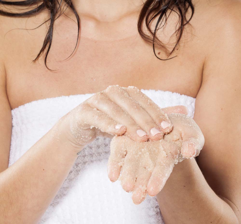 A woman is exfoliating her body with FarmHouse Fresh Sweet Cream Fine Sea Salt Body Polish for soft and nourished skin.