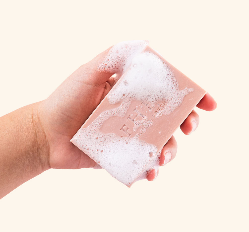 A hand holding a bar of softly scented FarmHouse Fresh Sweet Tea Shea Butter Bar Soap with rich lather on it.