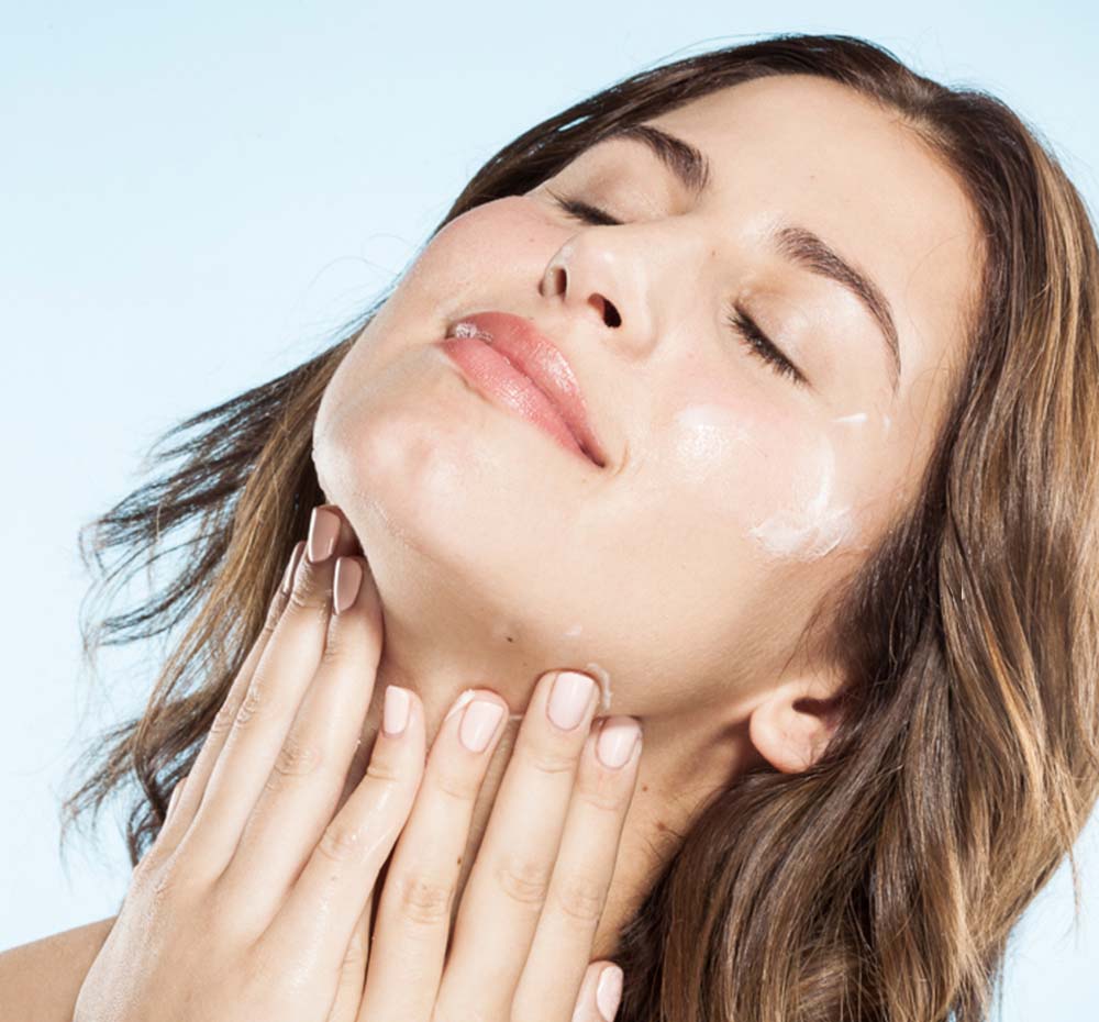 A woman is applying FarmHouse Fresh Three Milk Ageless Sleep Cream on her face and neck to delivers softness, illumination, and firmness to skin.