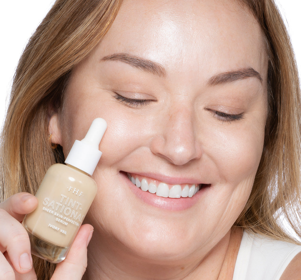 Tint-sational Sheer Skin-Perfecting Serum applied on woman's face holding bottle of shade Ivory Veil