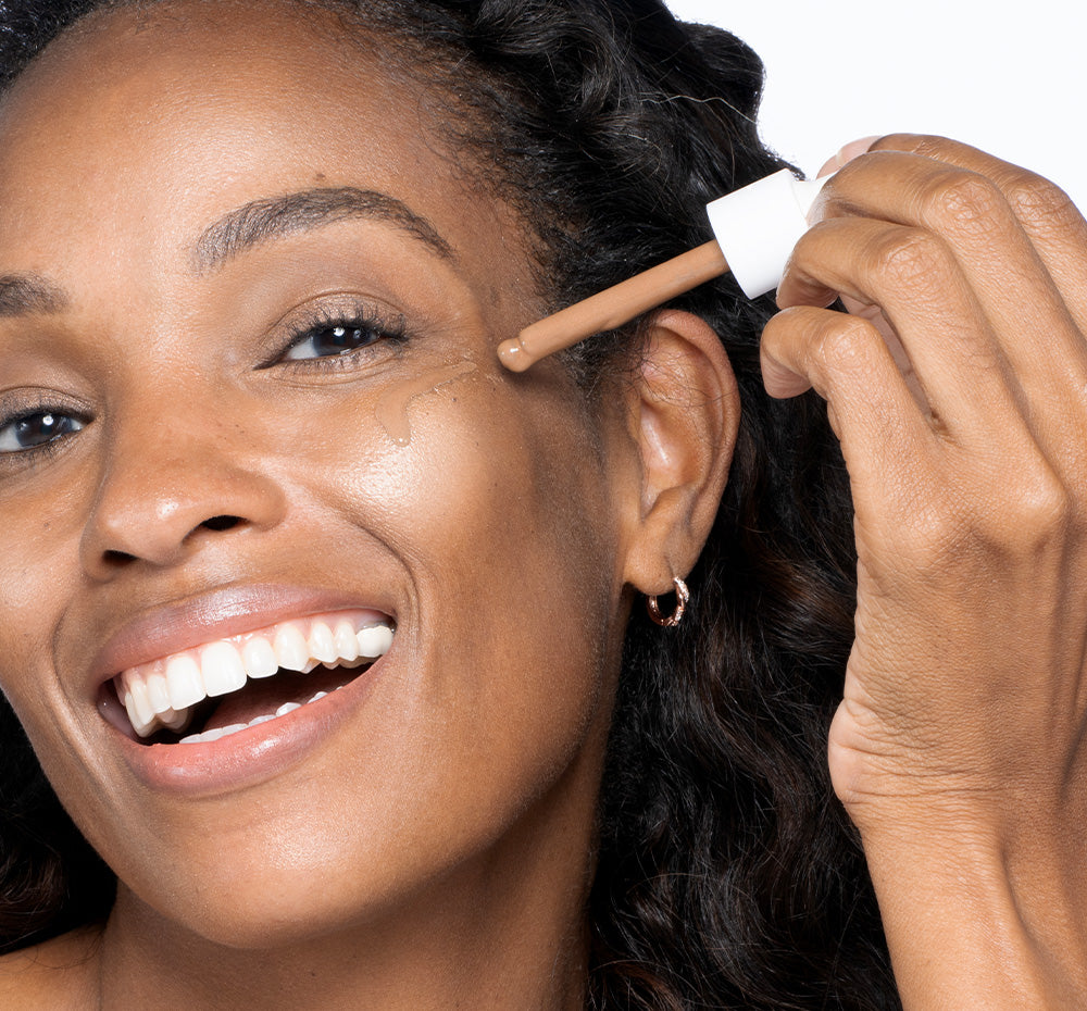 Woman applying Tint-sational Sheer Skin-Perfecting Serum on face using dropper, using Rich Cocoa shade.