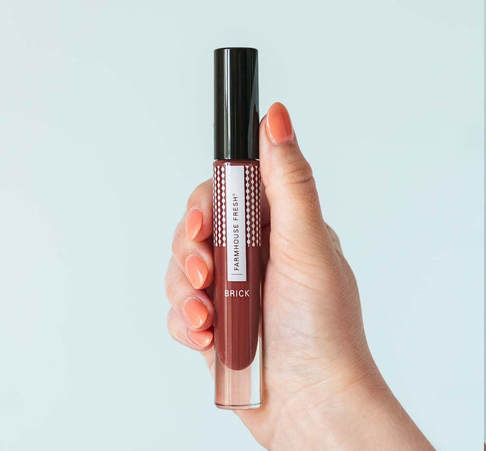 A hand holding FarmHouse Fresh Vitamin Glaze Oil Infused Lip Gloss in Brick color.