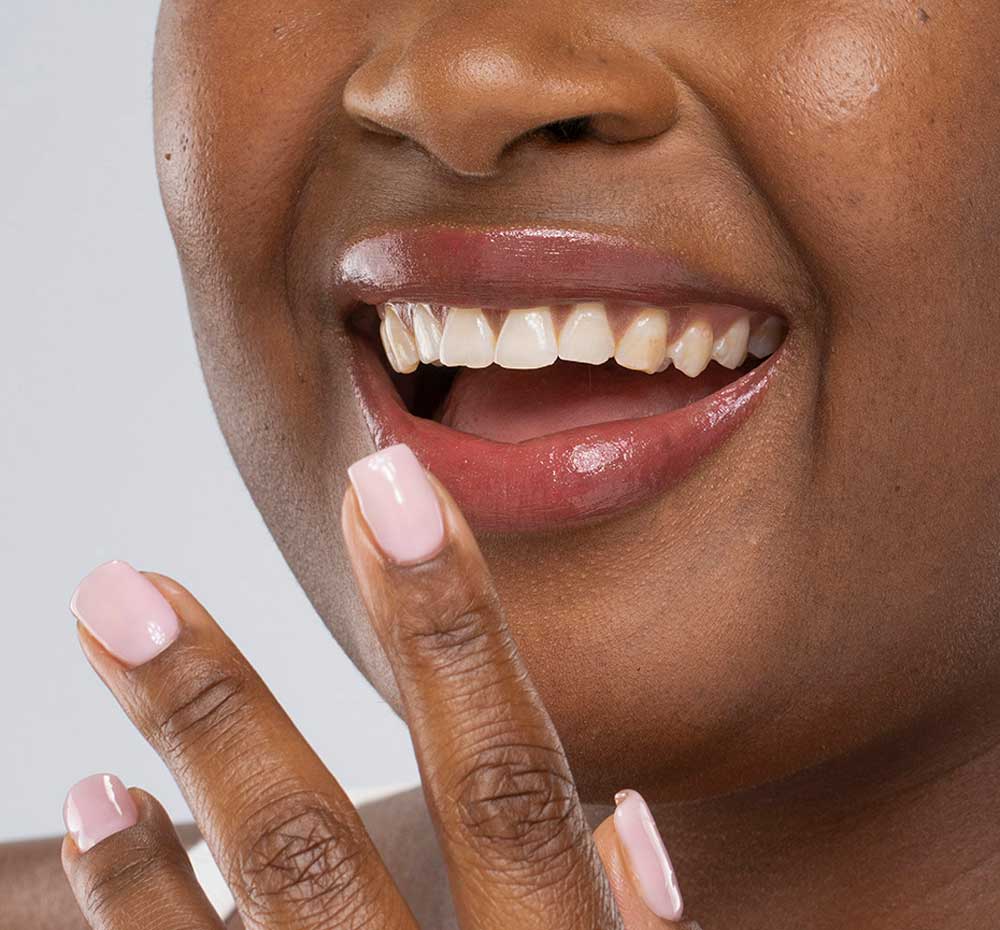 A smiling woman with FarmHouse Fresh Vitamin Glaze Oil Infused Lip Gloss in Brick color on her lips, demonstrating the neutral & earthy color.