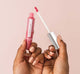 A hand holding FarmHouse Fresh Vitamin Glaze Oil Infused Lip Gloss in Sheer Pink color.