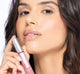 A woman is holding FarmHouse Fresh Vitamin Glaze Oil Infused Lip Gloss in Delicate Rose color, demonstrating the bright and sassy color.