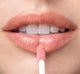 A woman is applying FarmHouse Fresh Vitamin Glaze Lip Gloss in Peach Peony color that brings color to lips.