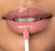 A woman is applying FarmHouse Fresh Vitamin Glaze Lip Gloss in Peach Peony color that hydrates lips.