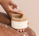 A woman is exfoliating her legs with FarmHouse Fresh Whipped Honey Fine Sea Salt Body Polish to polish away dead skin cells and restore skin's hydration.