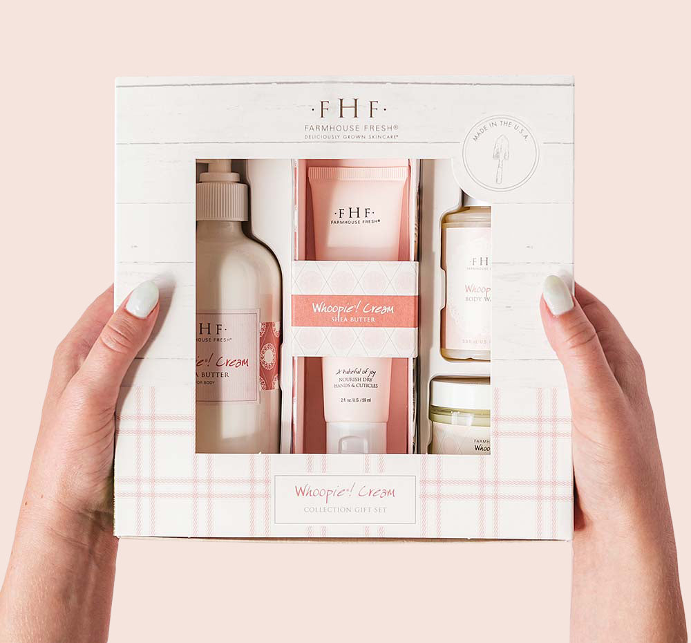 Hands holding a FarmHouse Fresh Whoopie Cream Deluxe Boxed Gift Set that includes a full-size body cream and hand cream, travel-size body wash and candle.