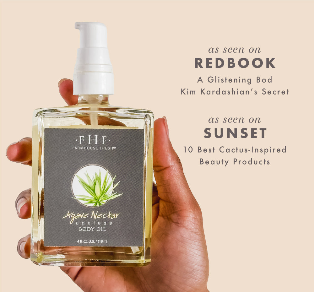 Hand holding a bottle of FarmHouse Fresh Agave Nectar Ageless Body Oil with media mentions about the product on a beige background.