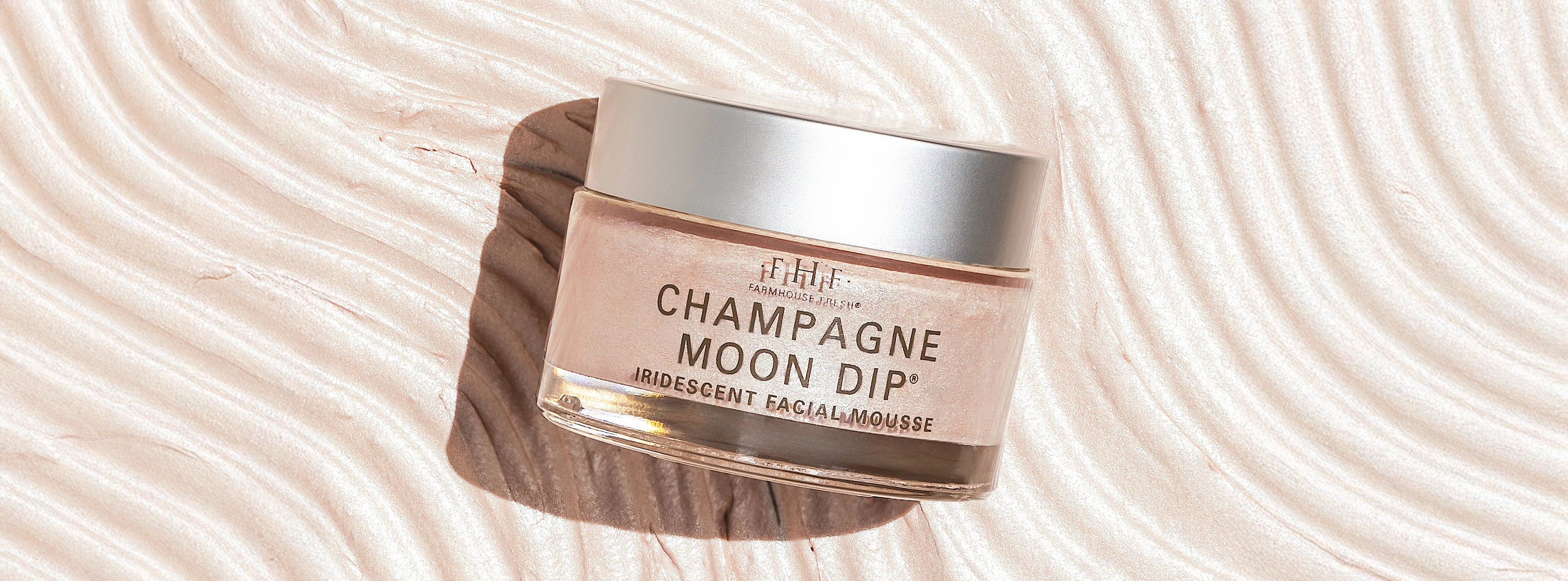 Facial mousse jar labeled 'Champagne Moon Dip' on a textured product swipe background