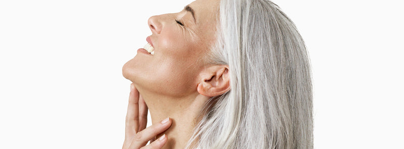 Woman with gray hair touching her face against a white background