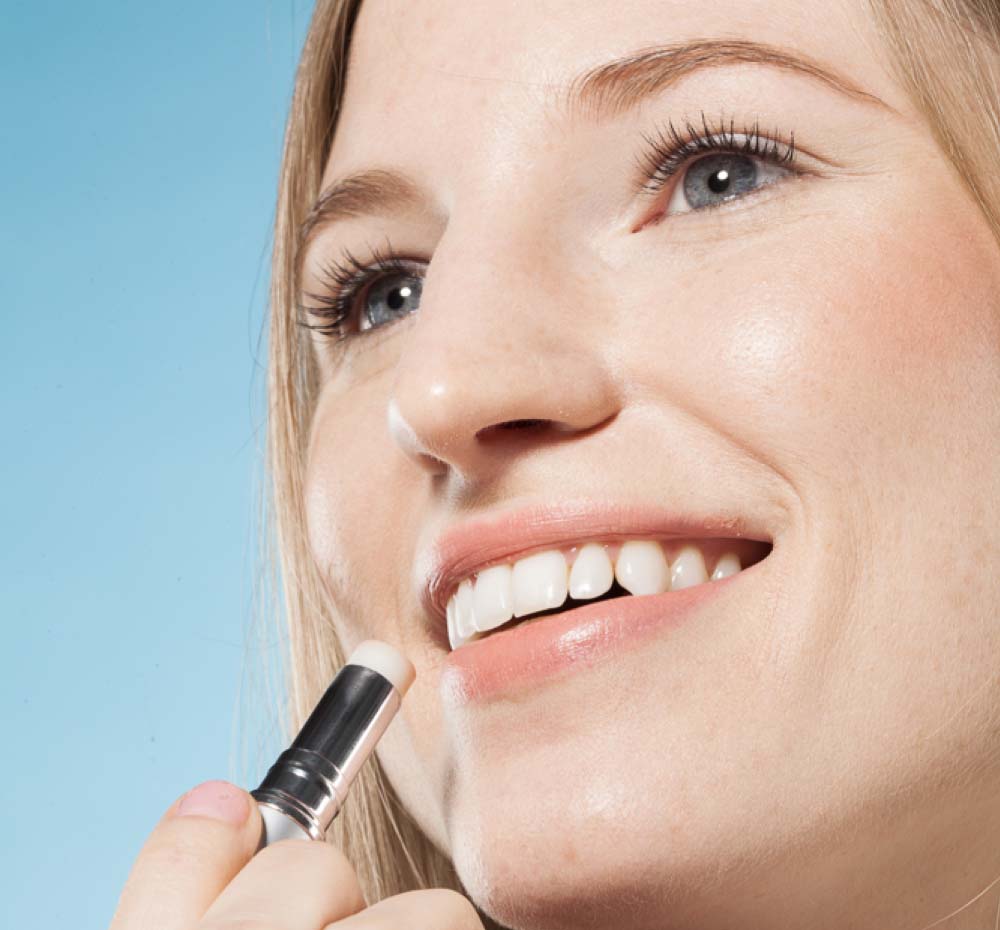 A woman is applying Farmhouse Fresh's Blackberry Crush lip balm from Blackberry Lip Gift Basket for dry and chapped lips.