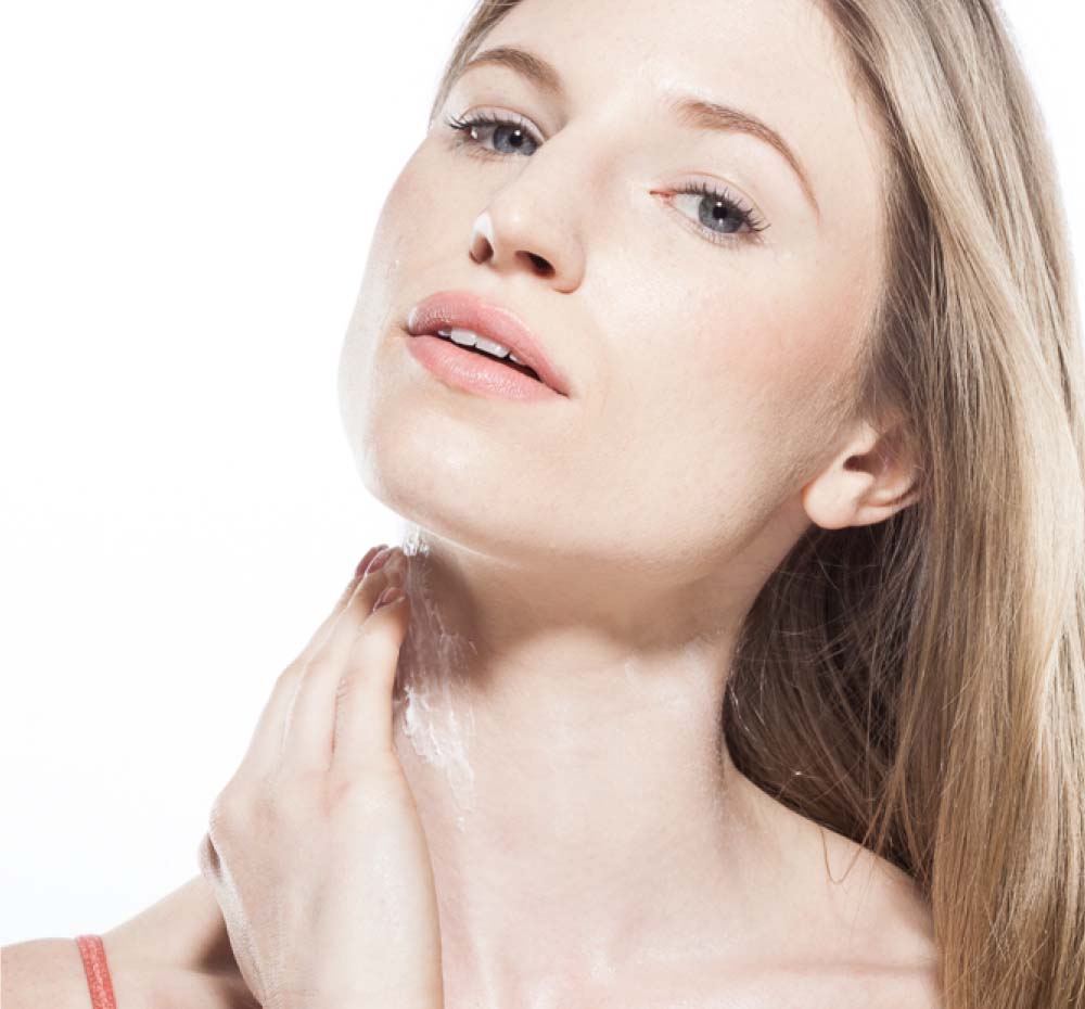 A woman is applying body mousse on her neck, demonstrating the age-fighting benefits of Blissed Moon Dip by Farmhouse Fresh.