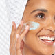 A woman is applying FarmHouse Fresh Bluephoria Chill-Out Super Moisture Mask on her face to improve the look of uneven skin tone.