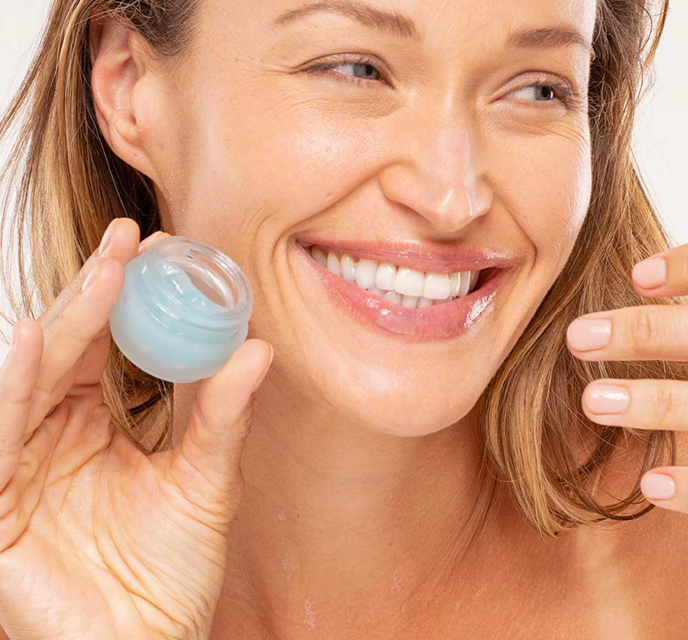 A woman is holding a jar of FarmHouse Fresh Bluephoria Lip Drench Jelly Sleep Mask, showing her moisturized, rejuvenated lips.