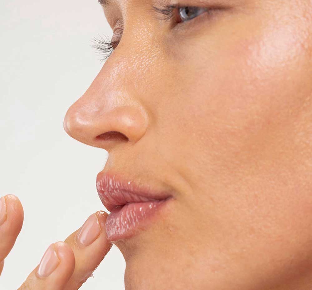 A woman is applying FarmHouse Fresh Bluephoria Lip Drench Jelly Sleep Mask to restore dry, cracked lips.