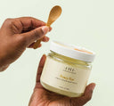 Hands holding a wooden spoon and a jar of Brandy Pear Liquor Infused Body Polish, a nourishing and natural body scrub.