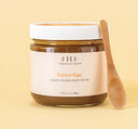 A jar of Farmhouse Fresh Butter Rum body scrub with a wooden spoon next to it.
