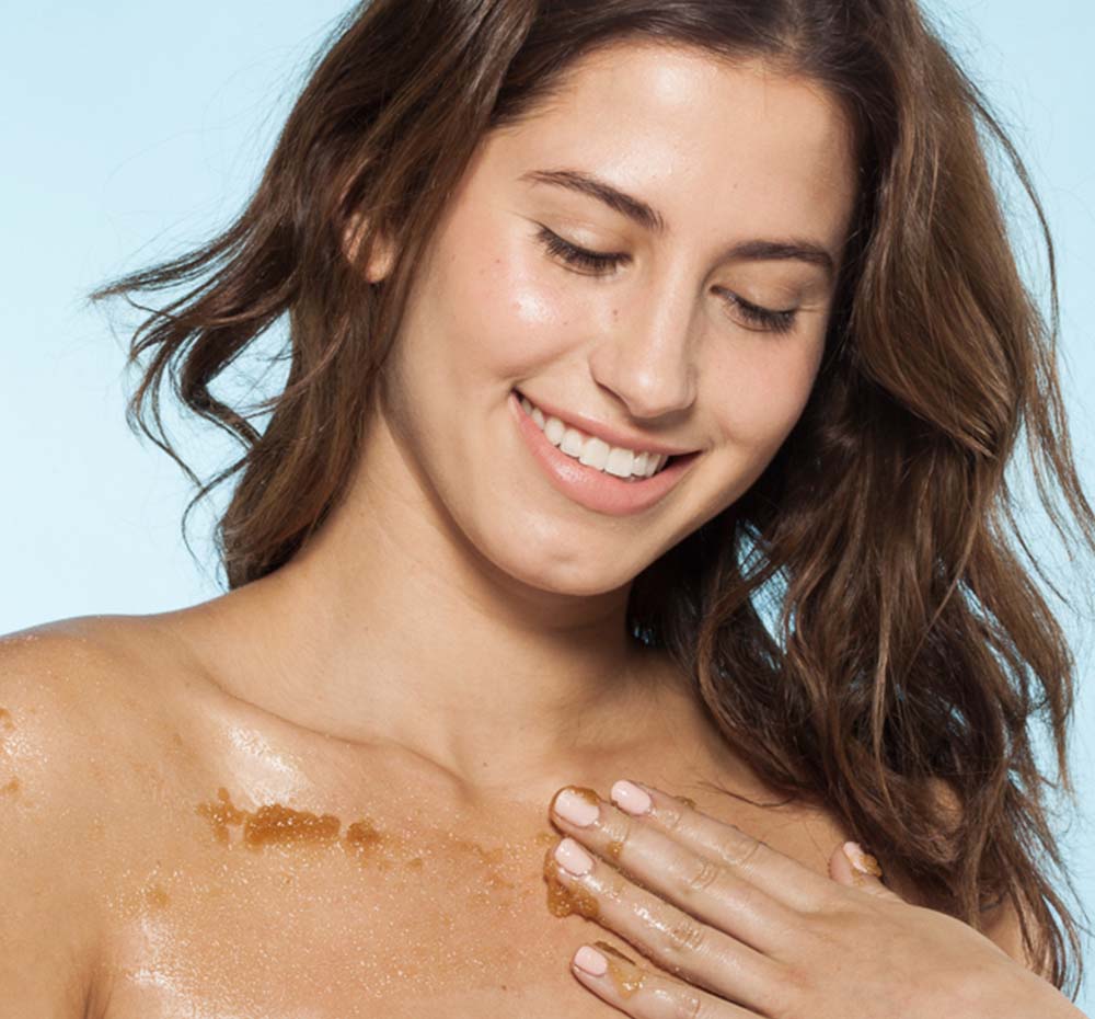 A woman with Farmhouse Fresh Liquor Infused Body Polish on her chest, exfoliating dry, rough skin.